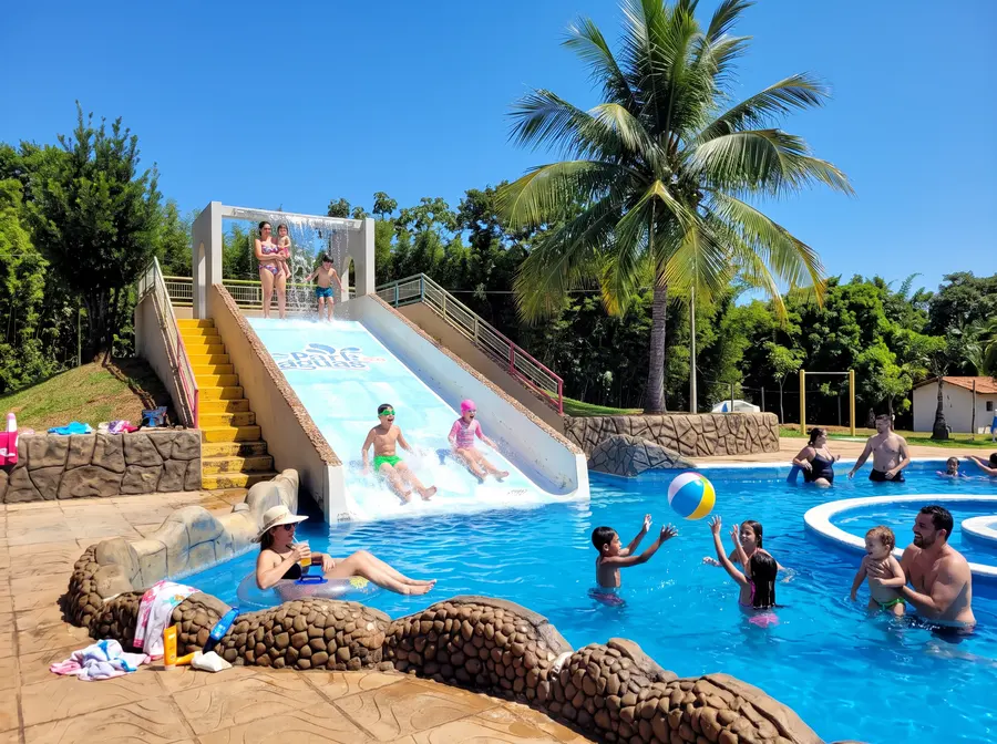 Escorregadores largos descendo para a piscina, entre coqueiros