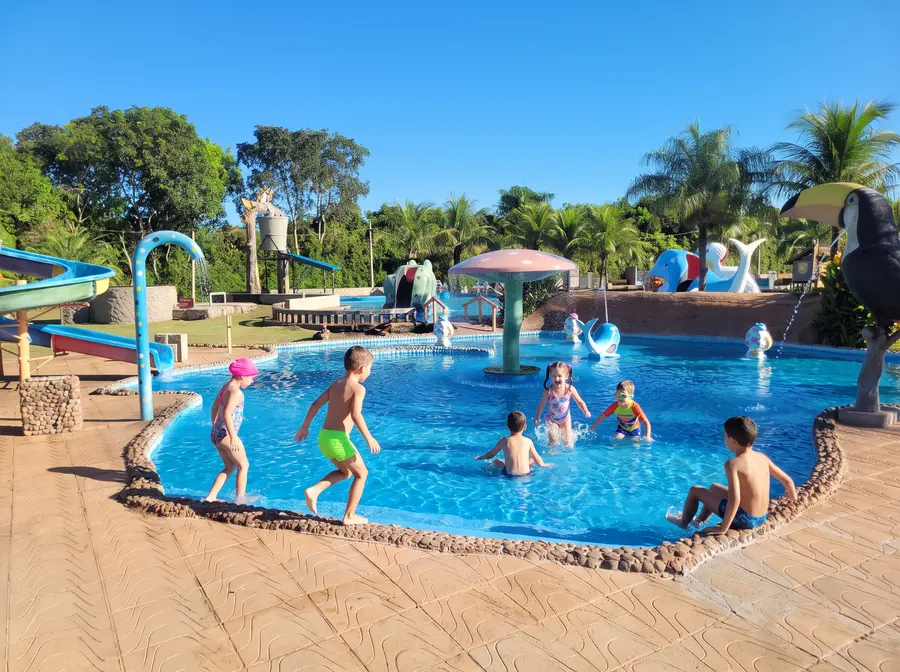 Piscina infantil rasa com chuveirões em forma de flor e crianças brincando